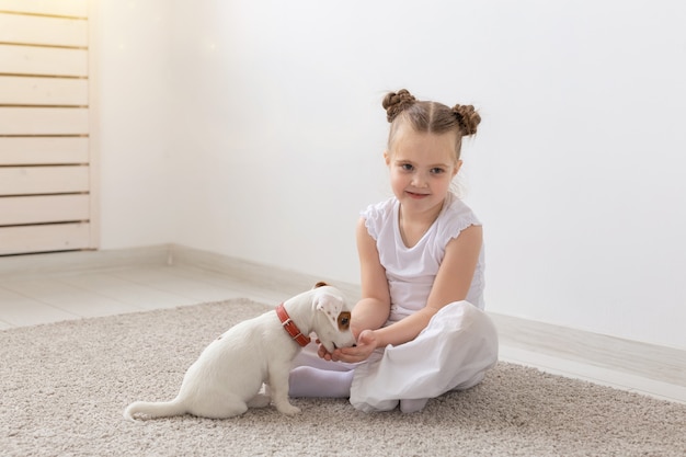 Children, pets and animals concept - little child girl in pajamas playing with Jack Russell Terrier puppy on the floor