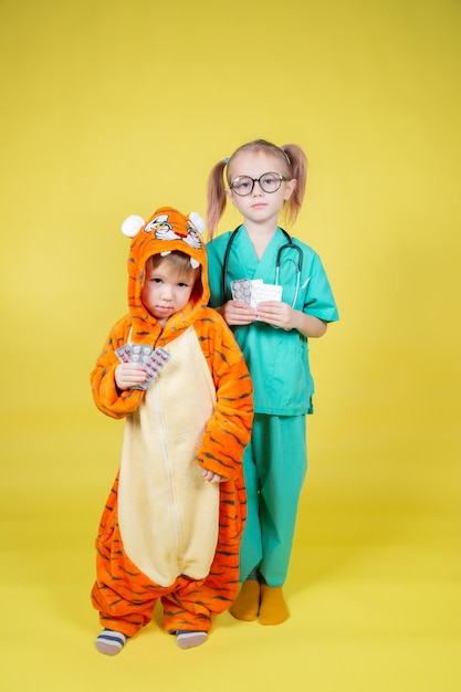 Children play doctor, a girl dressed as a doctor and a boy dressed as a tiger hold blisters with pills in their hands