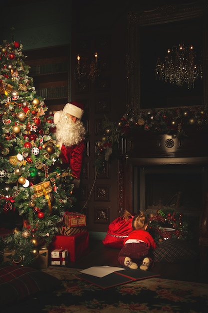 Children play near the Christmas tree. The real Santa Claus is watching them.