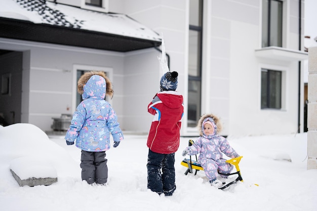 Children play outdoors in snow Three kids enjoy a sleigh ride Child sledding in winter against house