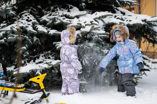 Children play outdoors in snow Two little sisters near Christmas tree in winter