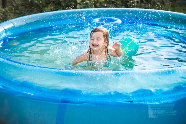 暑い夏には、子供たちはプールでボールで遊ぶ。少女と少年 。屋外のプールでかわいい女の子