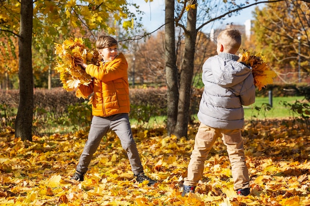 I bambini giocano con le foglie secche nel parco autunnale. gli amici dei fratelli si divertono in una giornata di sole.