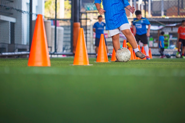 コントロールサッカーボールの戦術を遊んでいる子供たちは、背景を訓練するために芝生のフィールドでコーンサッカーで子供たちを訓練します