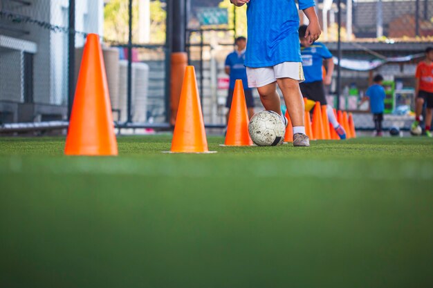 コントロールサッカーボールの戦術を遊んでいる子供たちは、背景を訓練するために芝生のフィールドでコーンサッカーで子供たちを訓練します