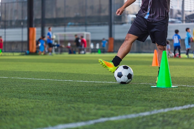 コントロールサッカーボールの戦術を遊んでいる子供たちは、背景を訓練するために芝生のフィールドでコーンサッカーで子供たちを訓練します