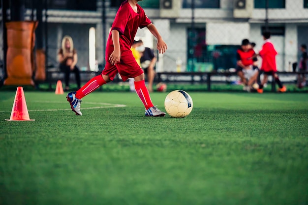 トレーニングの背景を持つ芝生のフィールドでコントロール サッカー ボール戦術コーンを遊んでいる子供たち