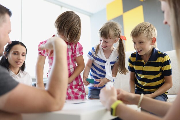 Children playing fun card game with adults brothers and sisters having fun at home with parents