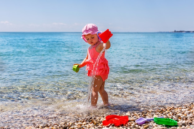 夏のビーチで砂のおもちゃで外で遊ぶ子供たち。かわいい幼児の女の子が水の海に立っています。テキスト用のスペースをコピーする