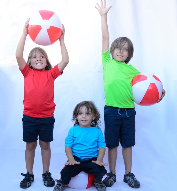 Дети позируют с пляжными мячами в разноцветных футболках