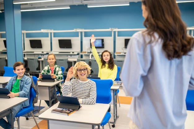 children raising their hands looking at teacher