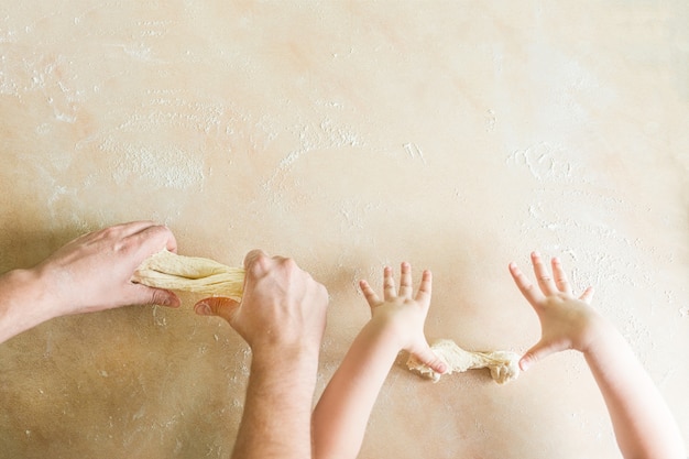 子供とお父さんの手が生の生地を作る