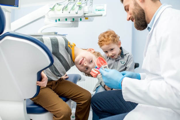 Dentista per bambini che mostra ai ragazzi come lavarsi i denti sulla mascella artificiale presso lo studio dentistico