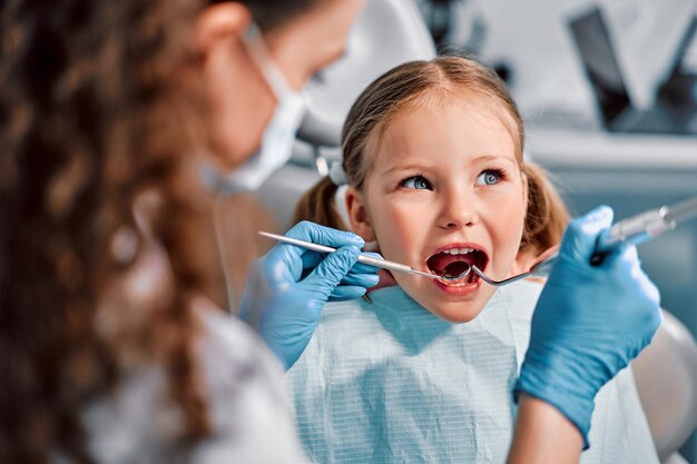 Foto odontoiatria infantile primo esame dal dentista una bella ragazza carina con la bocca aperta guarda di lato mentre il medico le cura i denti