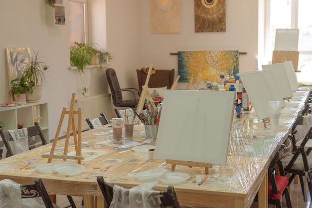 Children's drawing class. Easel, canvases, paints on the table. Waiting for students. Interior of the art school for drawing children.