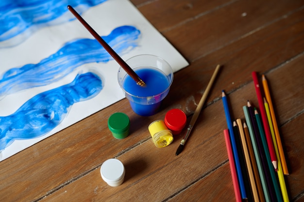 Children's drawing, paints and pencils on wooden table, workshop concept, nobody. Lesson at the art school. Work of young painter, pleasant hobby, happy childhood. Creative development