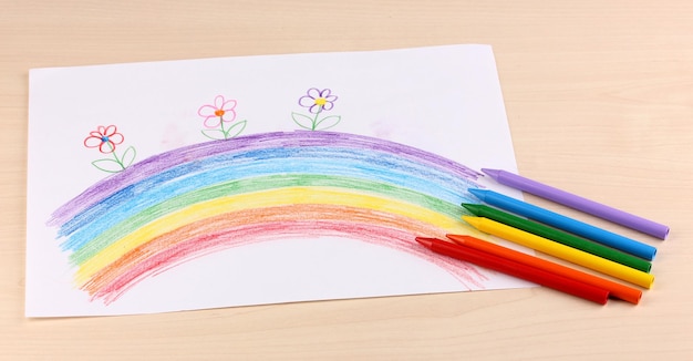 Children's drawing of rainbow and pencils on wooden background