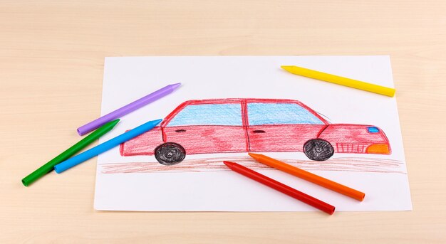 Photo children's drawing of red car and pencils on wooden background