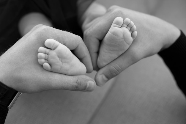 Children's feet in the hands of parents. Legs of a tiny newborn in the arms close-up. Family and chi