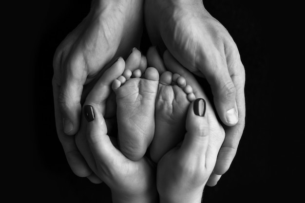 Photo children's feet in hold hands of mother and father on white. mother, father and newborn child. happy family people concept. black and white. high quality photo