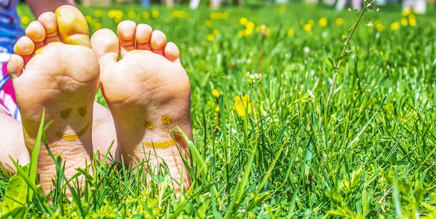 絵の具の模様が描かれた子供の足は、緑の芝生の上で微笑んでいます。セレクティブフォーカス。自然。