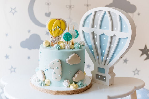 Children's first birthday cake, blue cake with clouds, meringue and balloons