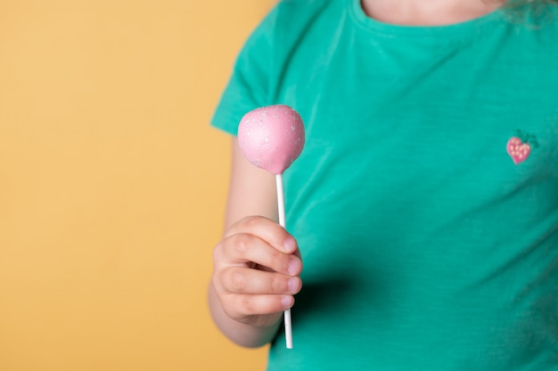 Photo children's hand holding pink cake pops. yellow wall.