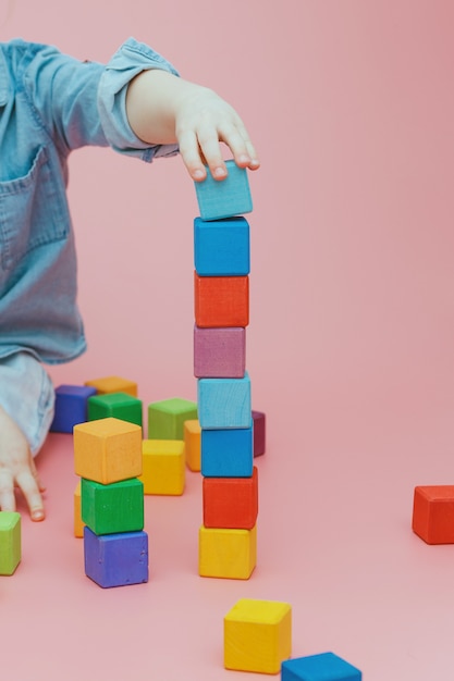 Children's hand is building a tower of wooden colored cubes.