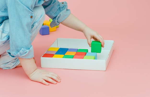 Children's hand takes wooden colored cubes from a white box.