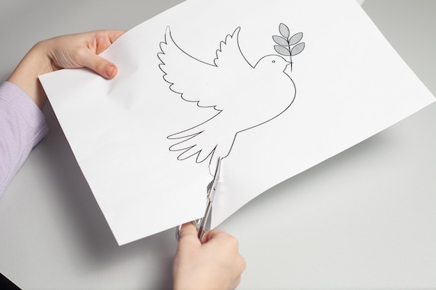 Children's hands are carving a crane on a white paper with small scissors.