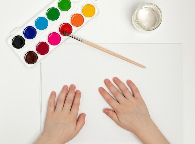 Children's hands begin to draw at a table with art supplies top view