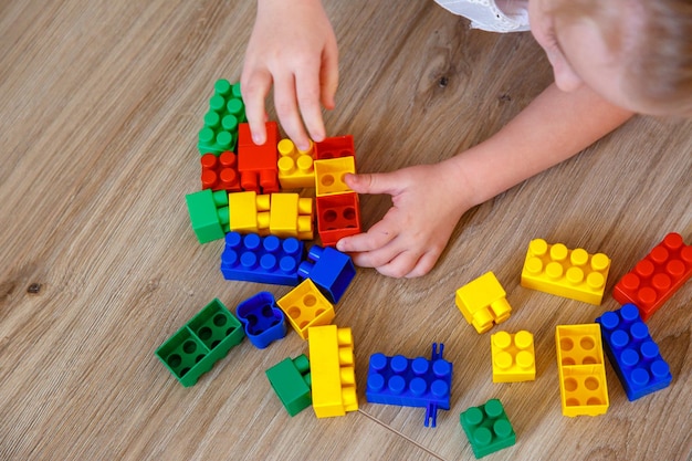 Детские руки ребенок играет в конструктор дома на полу