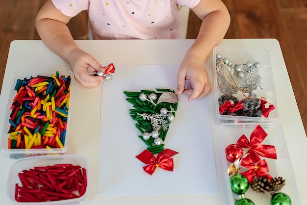 Children's hands creating Christmas tree from dyed pasta for the holiday of Christmas Sensory play for childs Holiday Art Activity for Kids material Montessori fine motor skills sensory bin