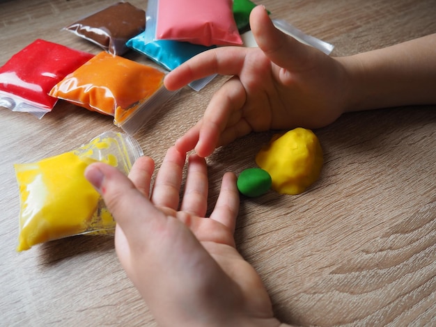 子供の手は柔らかい粘土をくしゃくしゃにします 粘土を含むパッケージはテーブルの上にあります 手の細かい運動能力を開発するための創造性 粘土から金型またはモデルを作成する