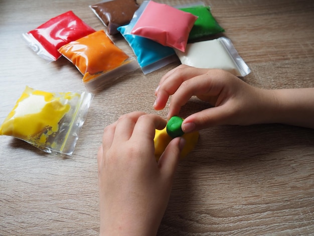 어린이 손은 부드러운 플라스틱을 구겨줍니다 플라스틱이 포함된 패키지는 테이블 위에 있습니다 손의 미세 운동 기술 개발을 위한 창의력 플라스틱에서 금형 또는 모델 만들기