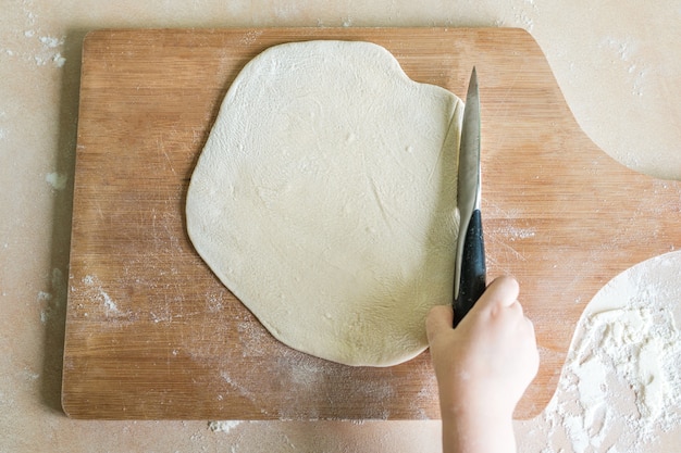 Children's hands cutting raw rolled dough