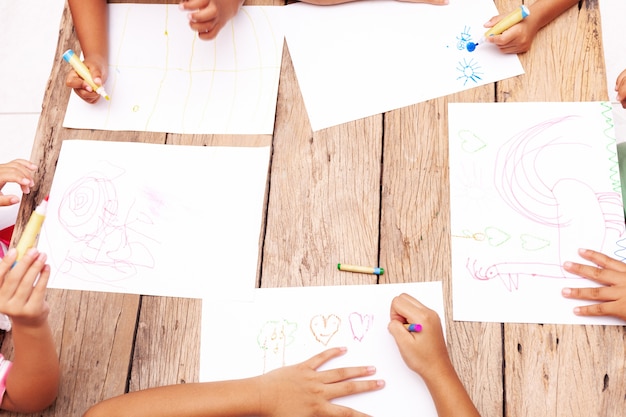 Children's hands drawing with colored pencils on wooden table