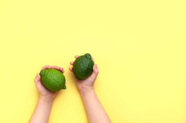 Children's hands hold two limes on a yellow background