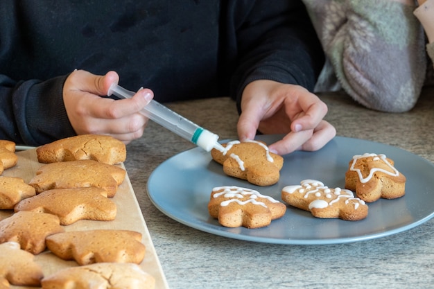 Foto le mani dei bambini preparano i biscotti di panpepato di capodanno su un tavolo di legno. fare i biscotti con un tagliabiscotti. anno nuovo e concetto di natale.