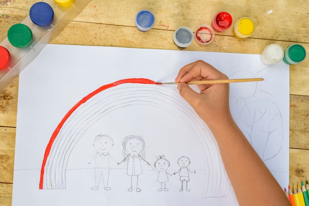 Children's hands paint a drawing with a brush and paints. Top view