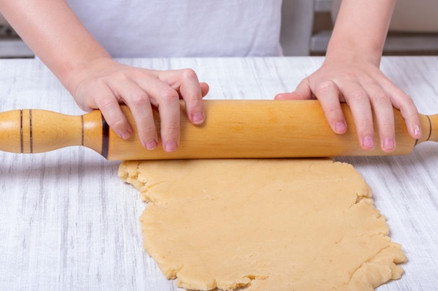 Le mani dei bambini stendere l'impasto con un mattarello sul tavolo in cucina, primo piano. il ragazzino aiuta la madre a cucinare facendo i biscotti fatti in casa. bambini che cucinano cibo fatto in casa