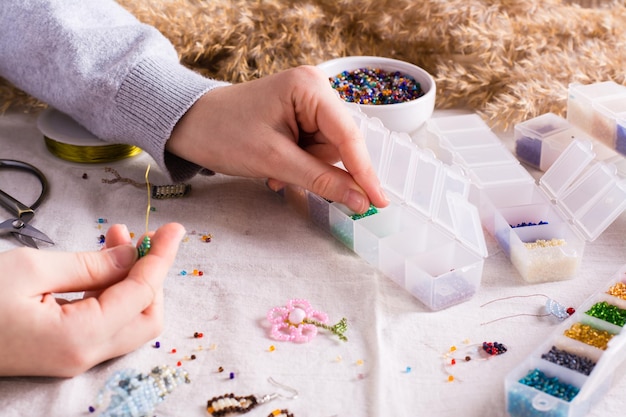 Children\'s hands take a bead and boxes with beads for weaving a\
bracelet