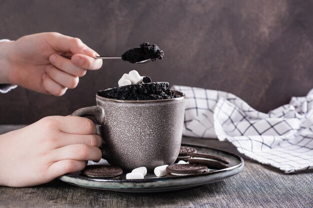 子供の手がマグカップからチョコレート ケーキを取り出して食べる