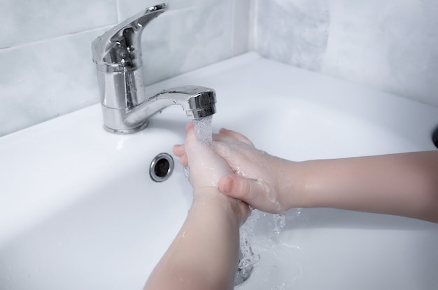 Children's hands under the tap in the bathroom. Hand hygiene.