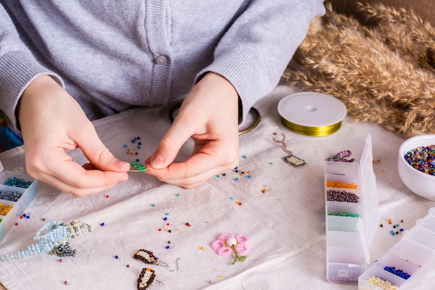 Children's hands weave a beaded toy on a table among boxes with beads Children's leisure