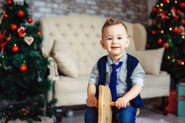 Children's joyful memories of Christmas holidays. Sweet stylish boy in a tie riding wooden rocking horse. Happy stylish little child.