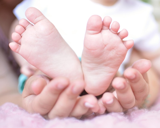 Photo children's legs in the hands of the mother tiny legs of a newborn baby on female hands closeup mom and her baby the concept of a happy family concept of health the treatment