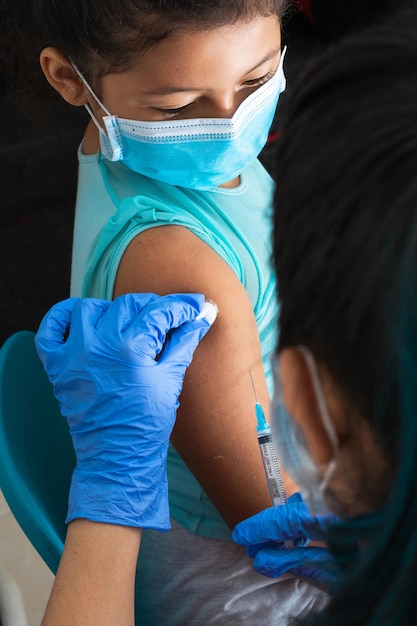 Children's nurse disinfecting brown girl's arm before administering injection, monkeypox vaccine