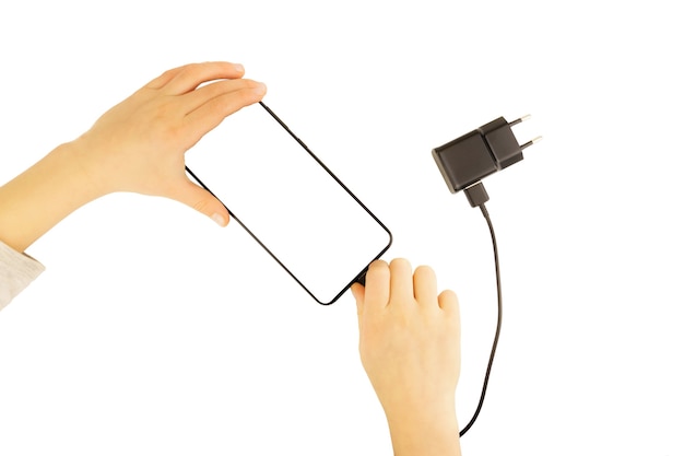 Children's pens insert the plug of the charger into a mobile phone, isolated on a white wall.