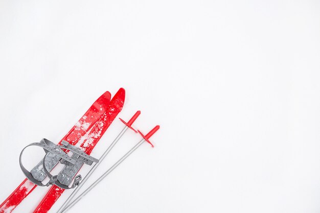 Children's red skis with sticks -layout in the snow. Children's winter sport, outdoor activities, family fun. White natural frosty background. Copy space.